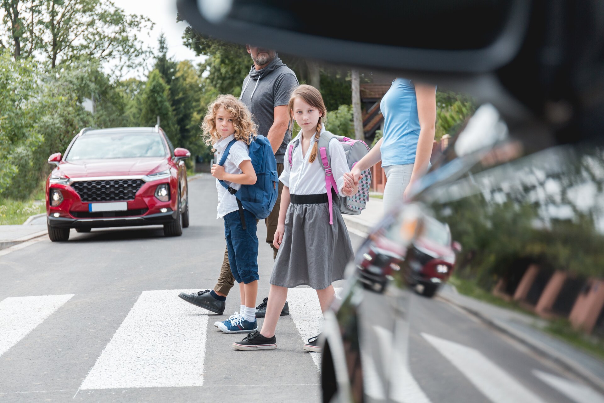 Gruppe von Schulkindern geht über den Zebrastreifen auf der Straße, direkt vor einem Auto.