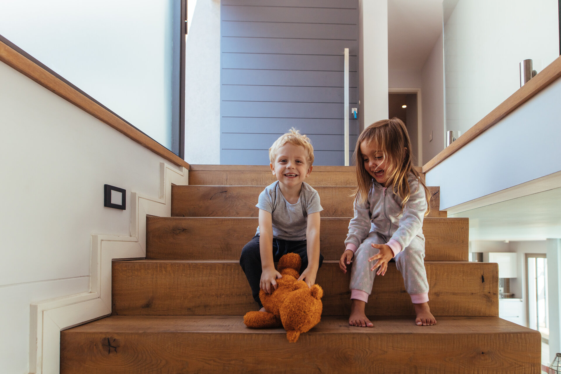 Kleine Kinder sitzen auf einer Treppe und der Junge greift nach einem Teddybär.
