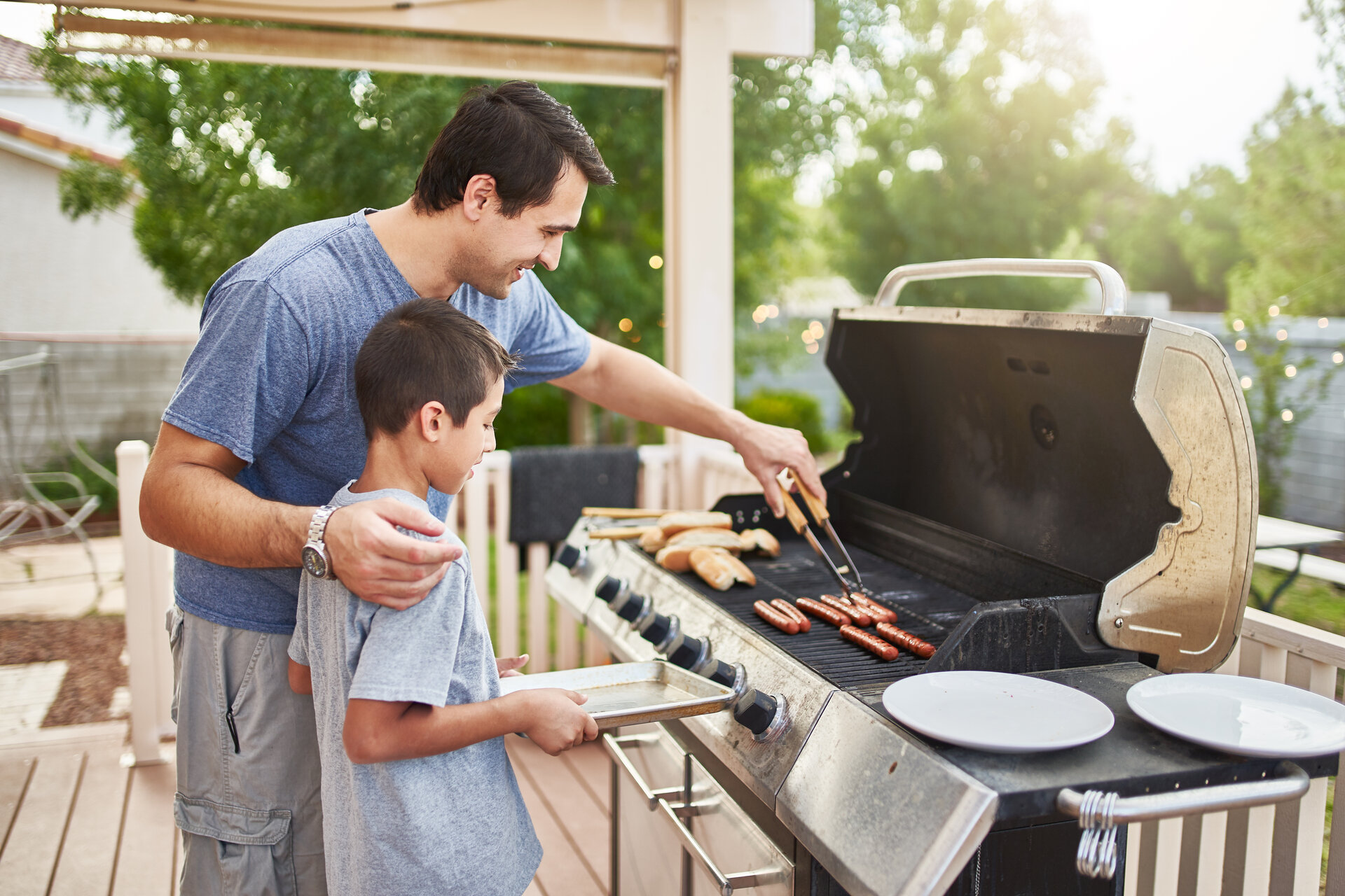 Vater bringt seinem Sohn bei, wie man draußen in der Aussenküche Hot Dogs grillt.