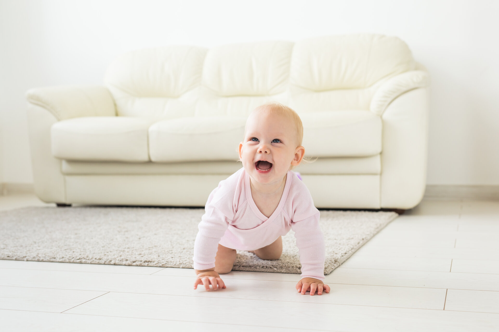 Porträt eines süßen Babys, das zu Hause auf dem Steinboden krabbelt und lacht.