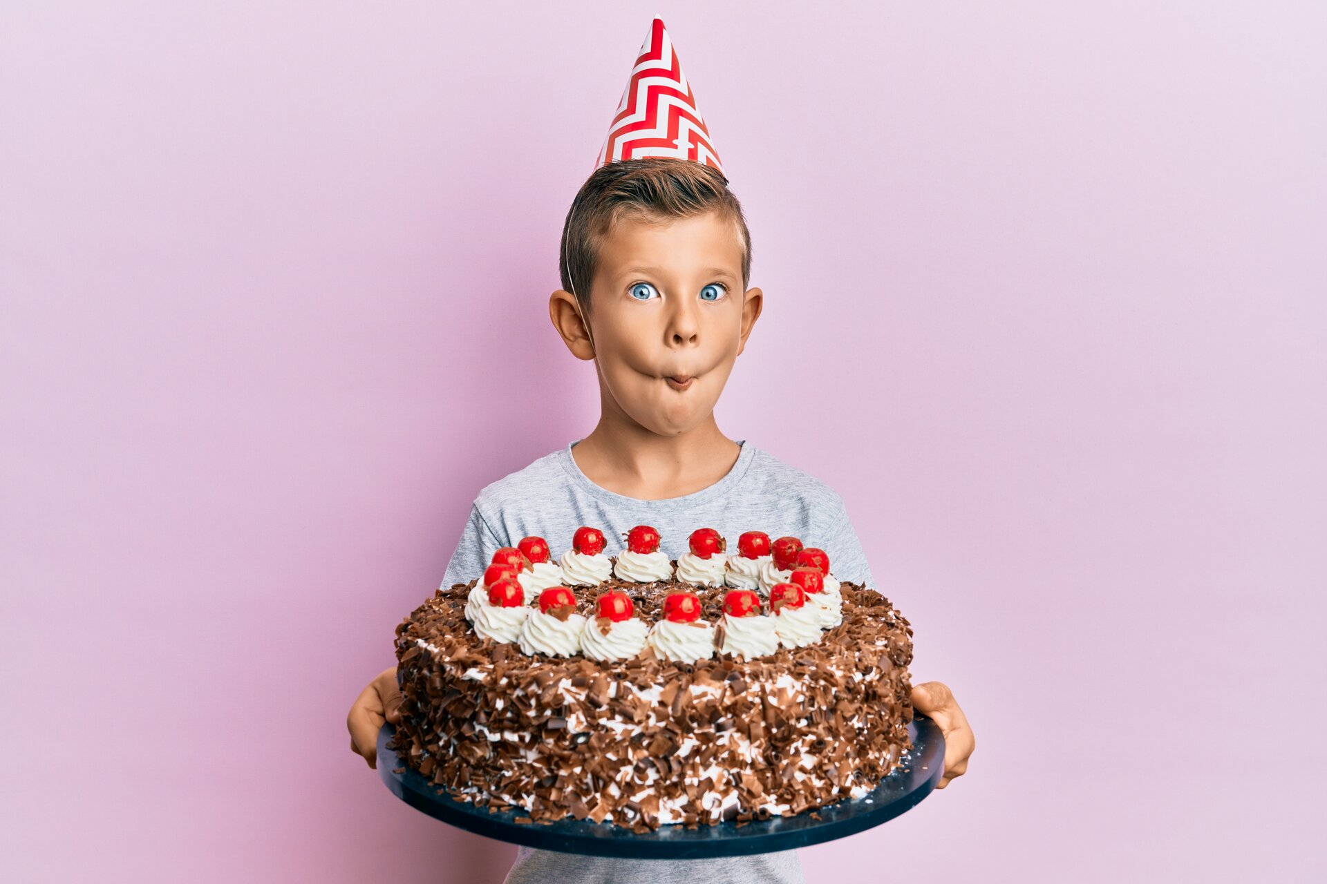Kind, das Geburtstag mit Kuchen feiert und Fischgesicht mit Mund und schielenden Augen macht.